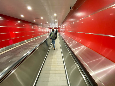 Large red modern long bright underground walkway between metro stations with travel walkers and escalators for quick passage of passengers.