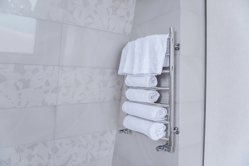 On an iron metal dryer holder, there are white terry towels for the shower. Hygiene, cleanliness concept. Marble tiles background in the bathroom. Trendy, fashionable interior. Copy space