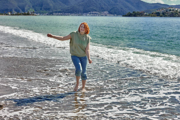 istock Young woman walks barefoot on beach in  surf zone. 1314413325