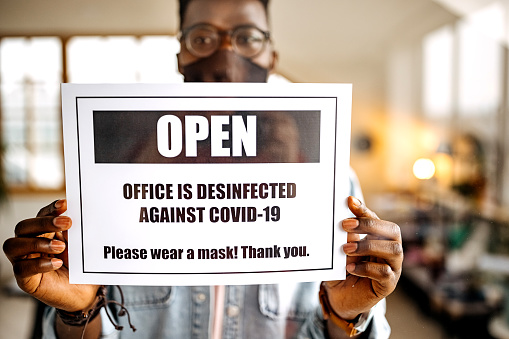Young casually clothed man putting open sign on front office door