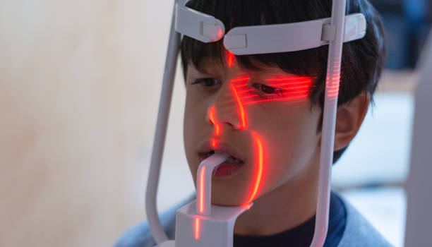 istock dark haired boy looking straight ahead placed on a panoramic dental x-ray machine with red lasers lighting his face with unfocused background 1314418858