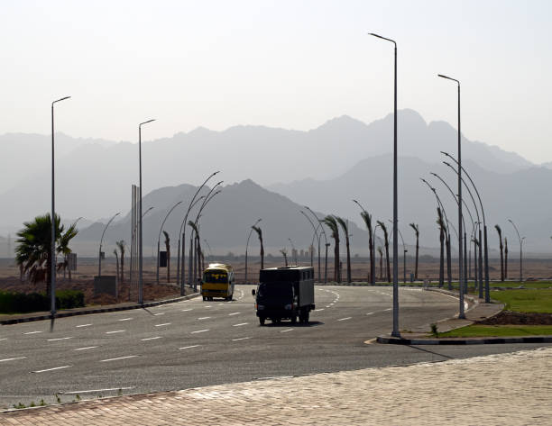 Two lonely buses drive along on empty asphalt desert road. Mountains and lampposts background. Resort town Sharm al-Sheikh, Egypt