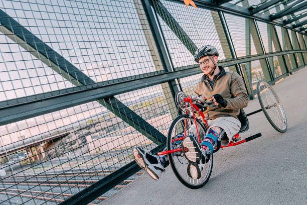 istock Handsome Young Man Riding a Red Handcycle Wearing Orthotic Leg Braces for Adaptive Exercise Outdoors on a Pedestrian Bridge in an Urban Sunset Setting 1314422812