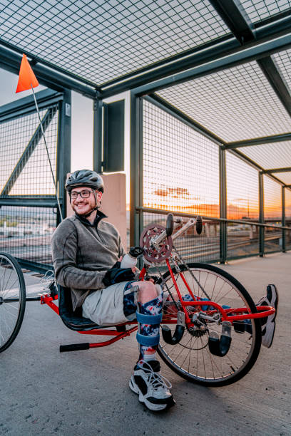 istock Handsome Young Man Holding a Water Bottle Looks Over His Shoulder While Sitting on a Red Handcycle Wearing Orthotic Leg Braces for Adaptive Exercise Outdoors on a Pedestrian Bridge in an Urban Sunset Setting 1314422815