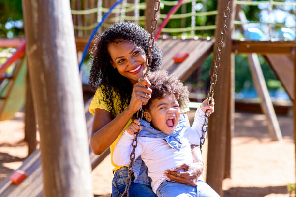 istock Daughter on mother's lap playing on swing in park 1314428255