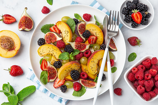Summer fruit and berry salad with chia seeds on white plate, marble baground, top view