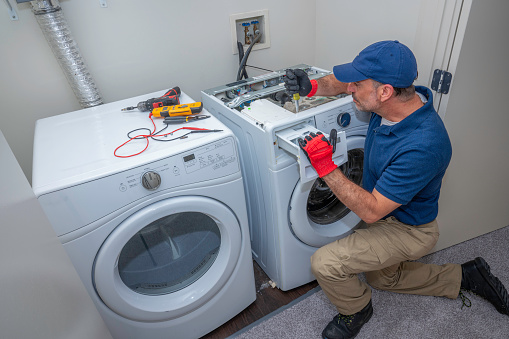 Técnico de electrodomésticos trabajando en una lavadora de carga frontal en una lavandería photo