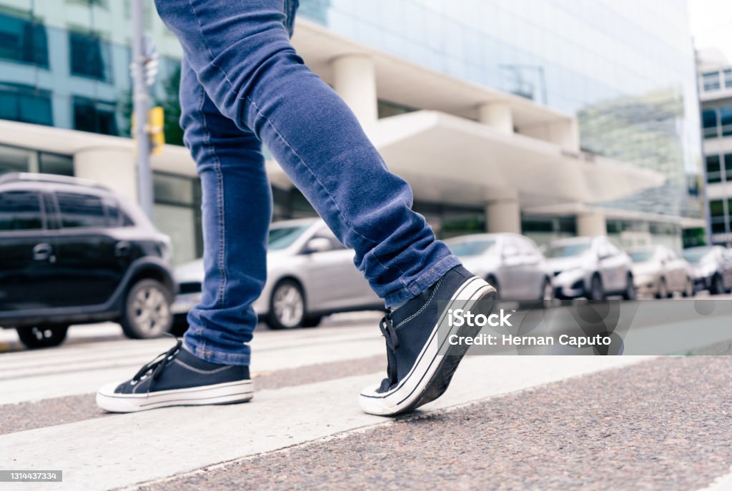 Close-up of the feet of a man in black sneakers crossing a street on the zebra or pedestrian path. Vial education Close-up of the feet of a man in black sneakers crossing a street on the zebra or pedestrian path. Pedestrian Stock Photo