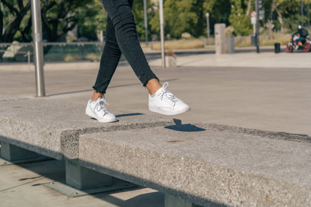 istock Slender female legs in white sneakers jumping between concrete blocks in a square. 1314438018