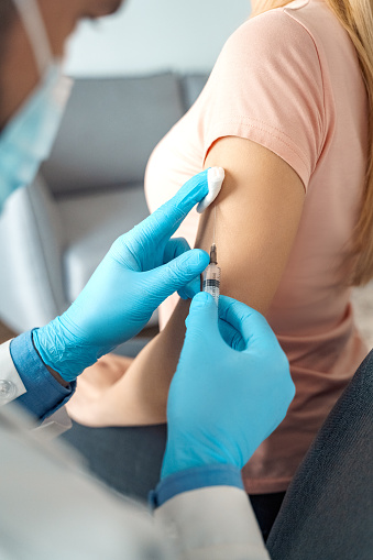 Putting vaccine on woman shoulder. Flu coronavirus covid19 vaccine. Man doctor vaccinating young caucasian patient with syringe putting injection to arm. Medical healthcare, disease prevention concept