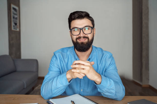 Smart man freelancer in eyewear looking at camera while sitting at desk stock photo