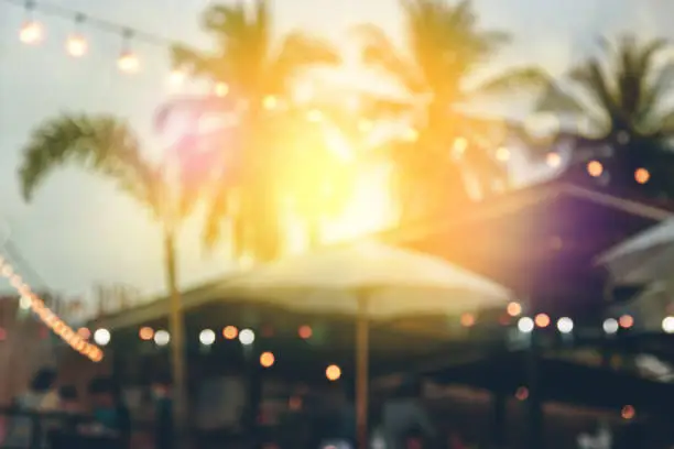 Photo of blurred bokeh light on sunset with yellow string lights decor in beach restaurant