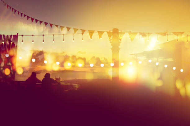 two friends watching sunset at restaurant on the beach, blurred bokeh light on sunset with yellow string lights decor in beach restaurant two friends watching sunset at restaurant on the beach, blurred bokeh light on sunset with yellow string lights decor in beach restaurant beach bar stock pictures, royalty-free photos & images