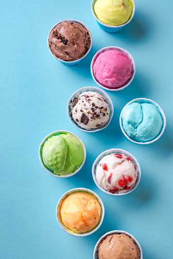 Ice Cream Assortment. Various ice creams or gelato on blue background, top view. Frozen yogurt  in small cups - healthy summer dessert.