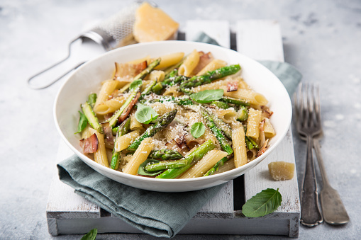 asparagus and bacon penne pasta with parmesan cheese in white bowl, selective focus