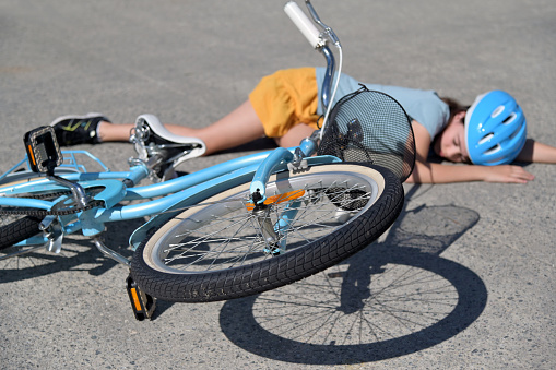 Young girl (female age 10-11) fallen of a bicycle laying down beside her bike unconscious on paved road. Above view.