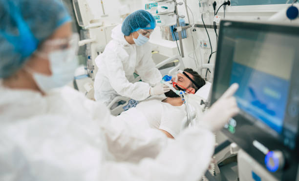 coronavirus covid-19 paciente infectado en una sala de cuarentena en el hospital con médicos en trajes protectores mientras hacen tratamiento de la enfermedad de él - ventilador equipo respiratorio fotografías e imágenes de stock