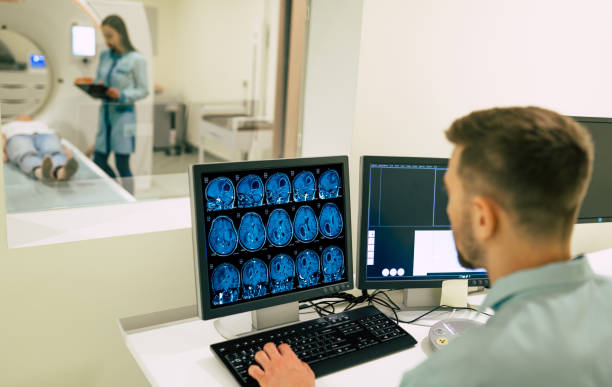 一名男醫生坐在電腦旁，用磁共振成像機觀察病人的後視照片 - 體檢 圖片 個照片及圖片檔