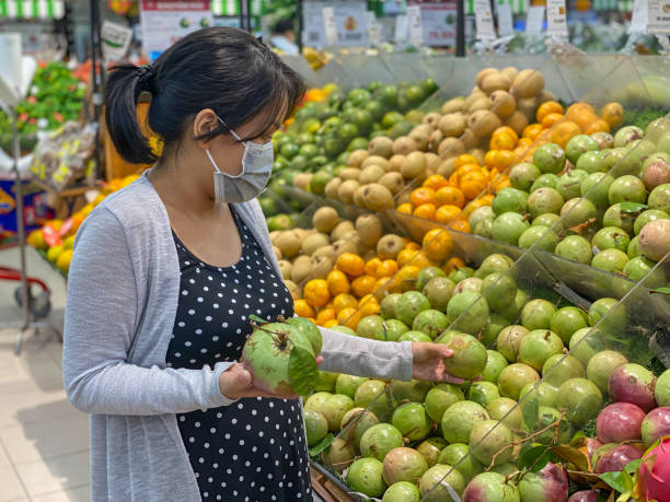 Asian woman buying tropical fruit at groceries store Rear view photo of Asian woman buying caimito or star apple fruit at supermarket chrysophyllum cainito stock pictures, royalty-free photos & images