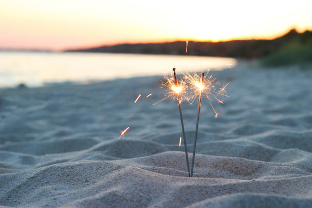 bengalas iluminan la arena cerca del mar sobre un fondo de puesta de sol - sparkler fotografías e imágenes de stock