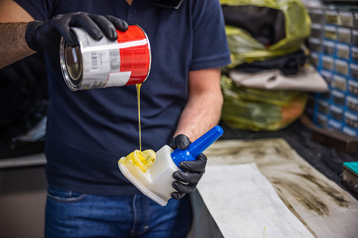 Midsection of man pouring glue into glue container, wearing protective gloves