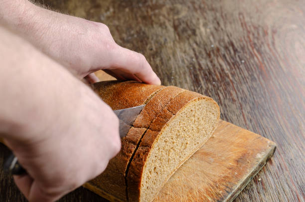 istock Hands slice bread on a wooden cutting board. 1314469406