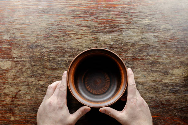 istock Brown earthenware bowl and hands on a wooden table. 1314469408
