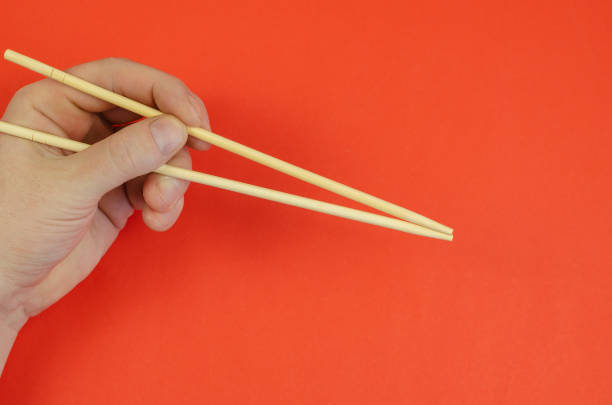istock A man's hand holds wooden chopsticks against a red background. 1314469431