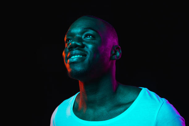 junge glückliche afroamerikanische mann isoliert auf dunklem hintergrund in neonlicht - neon fotos stock-fotos und bilder