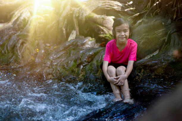 Kids sitting on timber or log tree in nature of waterfall