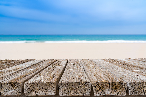 Empty rustic wooden table with defocused lonely white sand beach at background. Ideal for product display on top of the table. Predominant color are blue and brown. XXXL 63Mp outdoors photo taken with SONY A7rII and Zeiss Batis 40mm F2.0 CF