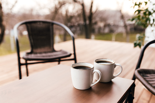 Two cups of coffee on the table on the wooden brown terrace during evening sunset. Relaxation, lovers romantic evening concept