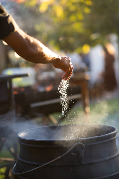 dodawanie grubej soli ręcznie do garnka z żelaznym kotła - africa african descent cooking african culture zdjęcia i obrazy z banku zdjęć