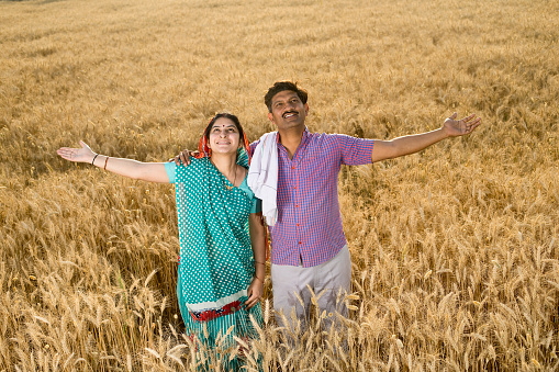 Happy rural couple with arms outstretched in agricultural field