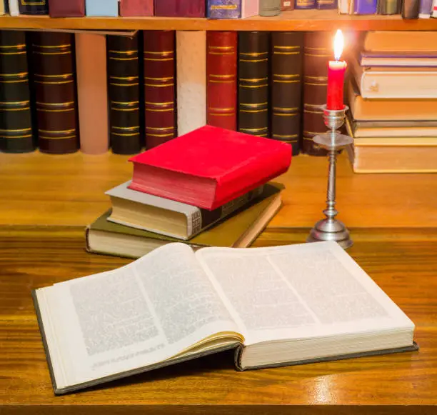 Photo of Open book on table against the other books by candlelight