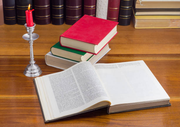 istock Open book on table against the other books, burning candle 1314475047
