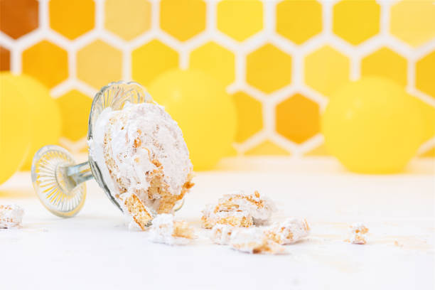 istock Smash birthday cake concept. A broken cake lying on an overturned stand. Yellow background with a decor in the form of a honeycomb and balloons. Copy space 1314475055