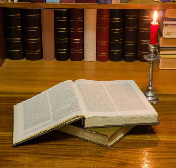 Photo of Open book on table against the other books by candlelight