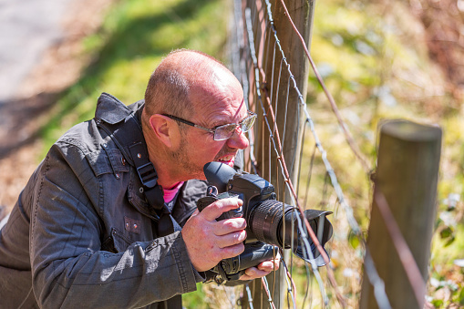 Male photographer shooting through fence in Welsh countryside