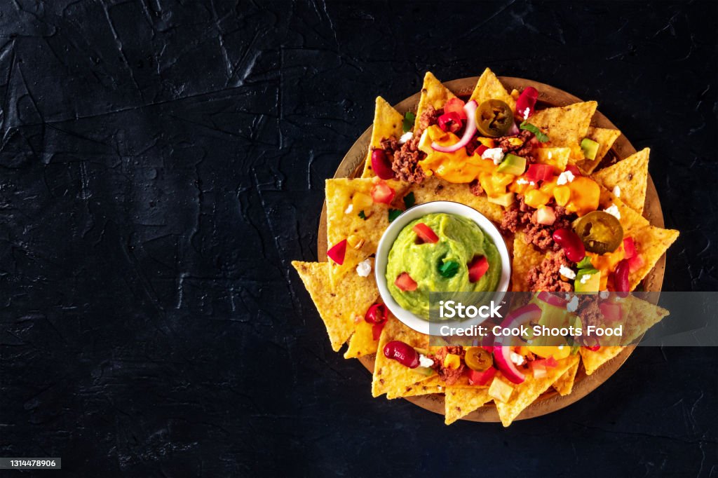 Mexcian nachos with beef, cheese sauce, and a guacamole dip, shot from above Mexcian nachos with beef, cheese sauce, and a guacamole dip, shot from above on a black background with a place for text Nacho Chip Stock Photo