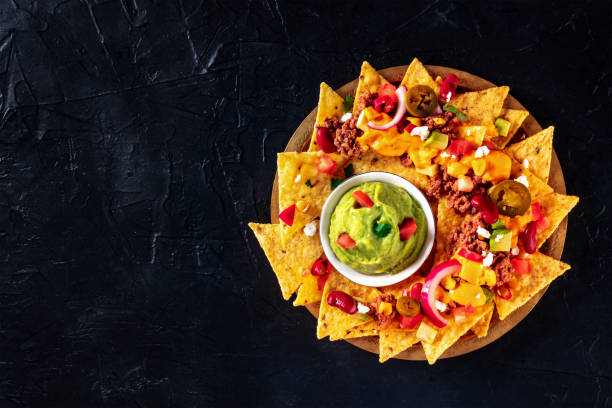 Mexcian nachos with beef, cheese sauce, and a guacamole dip, shot from above Mexcian nachos with beef, cheese sauce, and a guacamole dip, shot from above on a black background with a place for text nacho chip stock pictures, royalty-free photos & images
