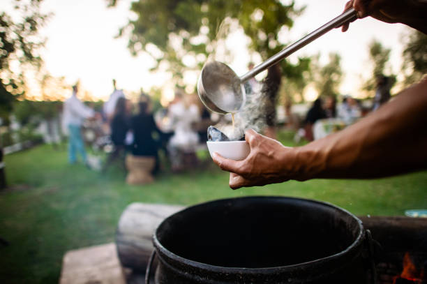 Dishing up warm mussels from a iron cauldron on a wood fire into a bowl with people in background Dishing up warm mussels from a iron cauldron on a wood fire into a bowl with people in background south african braai stock pictures, royalty-free photos & images