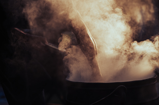Muscular Man Arm Silhouette Outdoor Street Food Preparation in an iron cauldron pot