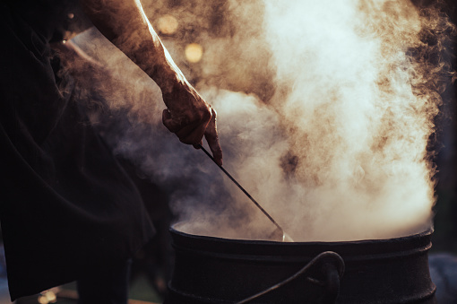 Muscular Man Arm holding spoon Silhouette Outdoor Street Food Preparation in an iron cauldron pot