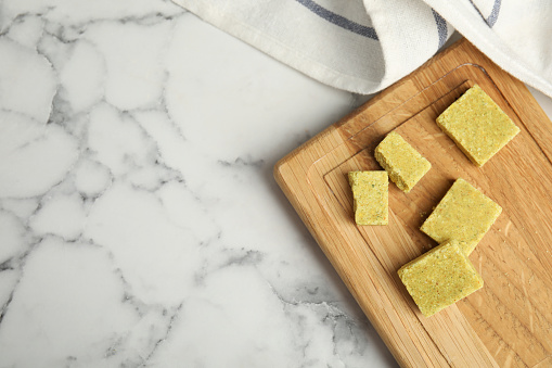 Bouillon cubes with wooden board on white marble table, top view. Space for text