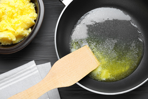 Frying pan and bowl with Ghee butter on dark wooden table, flat lay