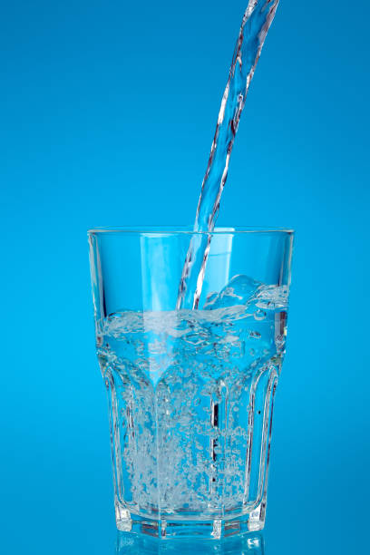 istock glass cup filled with a stream of fresh drinking water with bubbles and splashes, glassware for drinks glassful on a blue background with a gradient fill. 1314482041