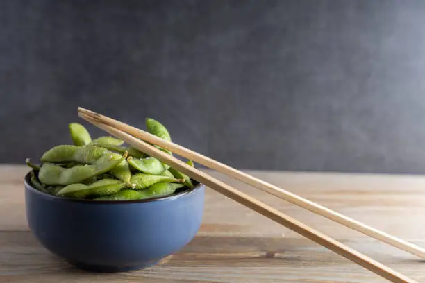 Japanese appetizer Edamame green soy beans seasoned with salt in a bowl, with shop sticks on the side.