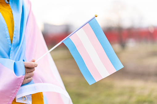 Transgender  covered with the transgender flag and holding a flag in the hand for defending her rights