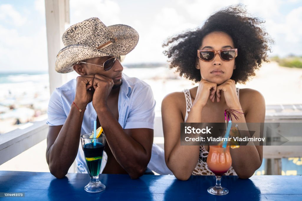 Young afro couple having arguments in their holiday on the beach Couple arguing each other during their vacation. They are standing bored and don't speak to each other Boredom Stock Photo